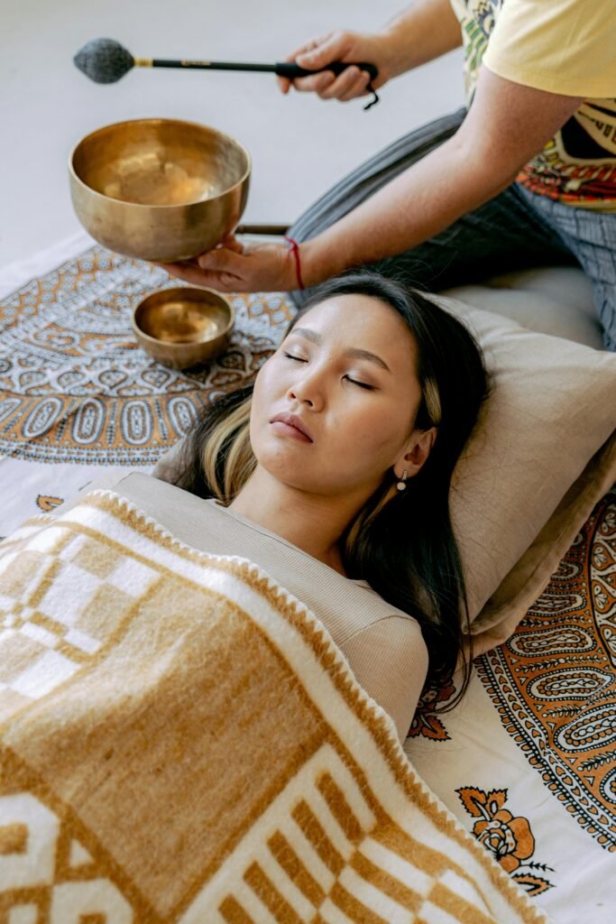 Asian woman enjoying a healing meditation with a Tibetan singing bowl indoors.