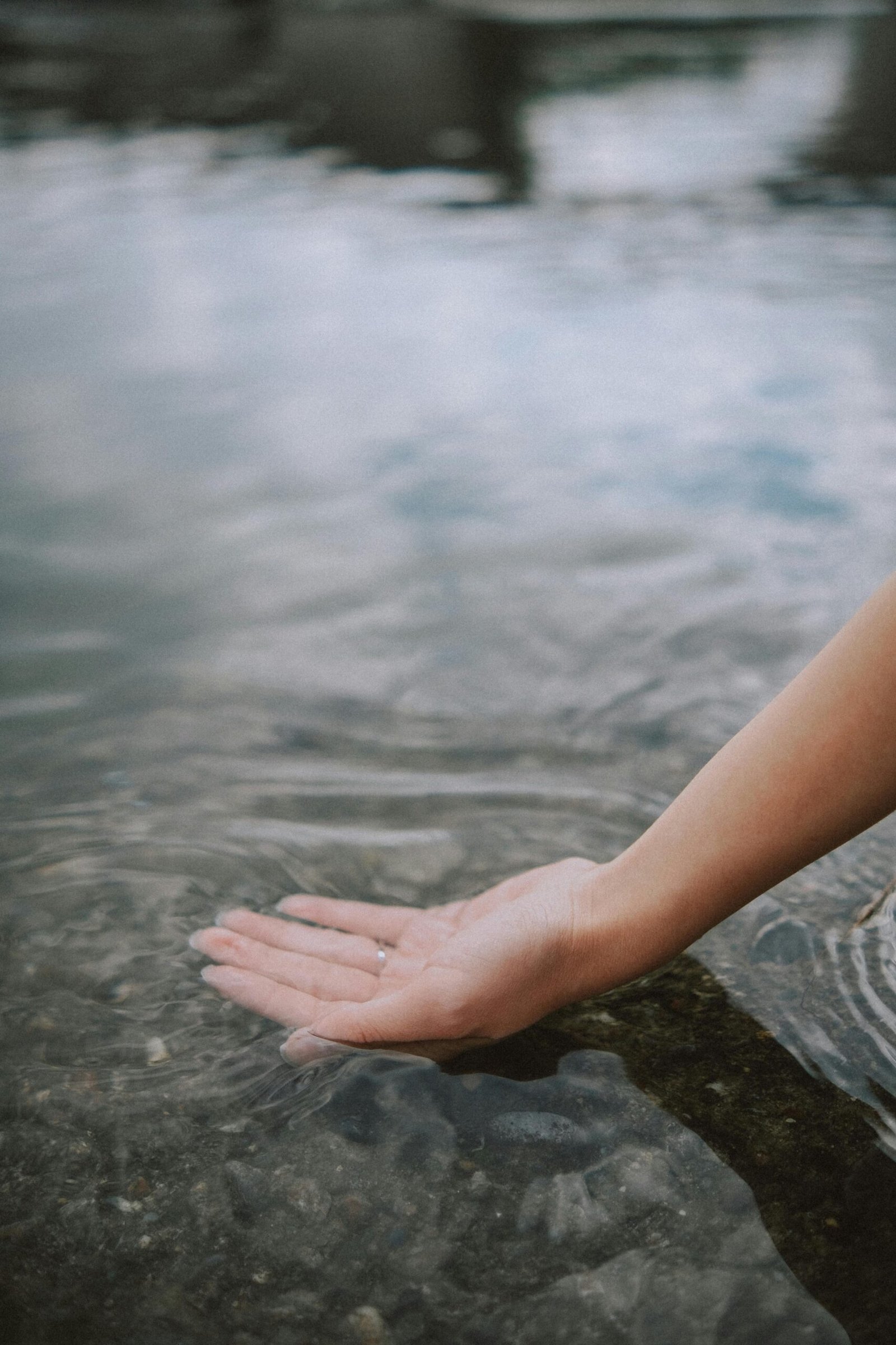 Close-up of a woman's hand gently touching a clear water surface outdoors, creating ripples.